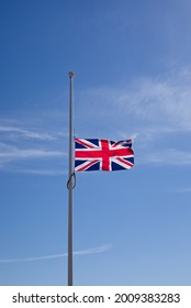 Portrait shot, Union Jack flag flying at half mast against blue sky representing national mourning or event