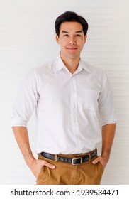 Portrait Shot Of Young Adult Asian Confident Man Model In Black Hairstyle Wearing Formal White Long Sleeve Shirt And Brown Pants With Hand In Pocket Posture Isolated With White Wall Background