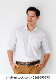 Portrait shot of young adult Asian man smiling in a formal white long sleeve shirt and brown pants with hand in pocket posturing looking at the side on white wall background in the studio. - Shutterstock ID 2169695893