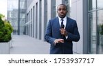 Portrait shot of young African American handsome male journalist talking with microphone for news episode outdoor. Pandemic concept. Man correspondent in suit and tie and with mic.