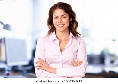 Portrait shot of young businesswoman wearing white shirt and looking at camera while standing in the office. 