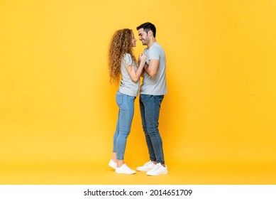 Portrait Shot Of Young Happy Interracial Millenial Couple Standing Close Looking In The Eyes And Holding Each Other Hands In Isolated Yellow Studio Background