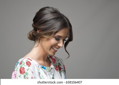 Portrait of shy timid smiling beautiful woman looking down expression over gray studio background.