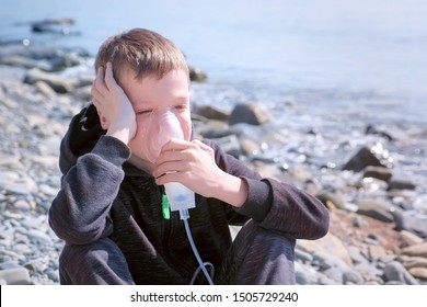 Portrait Sick 8y Child Boy Uses Nebulizer Sits On Seaside. Inhaling Inhaler Mask. Fibrosis Cystic Copd And Treatment. Asthma Pulmonary Respiratory Breath Problem Cure. Painkiller Sedative Gas Oxygen.