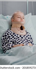 Portrait Of Sick Child Patient Lying In Bed Looking At Camera While Having Neck Cervical Collar Recovering After Painful Medicine Surgery In Hospital Ward. Kid Wearing Nasal Tube During Examination