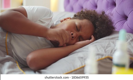 Portrait Of Sick Coughing African Boy Kid Lying In Bed At Home. Afro-american Ill Child With Severe Cough Lying In Bed At Home. Childhood, Healthcare And Medicine Concept