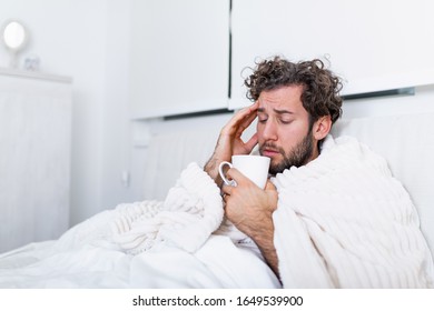 Portrait of a sick man with the flu, allergy, germs,cold coughing. Sick Man with headache sitting under the blanket with high fever and a flu, resting and drinking hot beverage