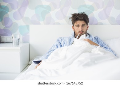 Portrait Of Sick Man With Thermometer In Mouth Reclining On Bed At Home