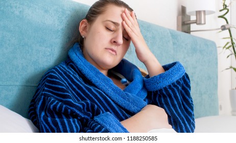 Portrait of sick woman with flue measuring temperature and holding hand on aching head