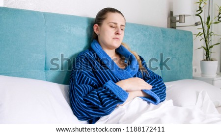 Portrait of sick woman lying in bed and holding digital thermometer under arm