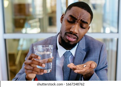 Portrait Of A Sick Young Man In Business Suit Taking A Medicine Pill With Water 