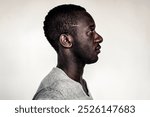 Portrait side view of a Black man, showcasing his strong features. This Black man stands against a neutral background, emphasizing his profile and expression. Portrait of black man side view