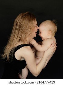 Portrait Side View Of Young Mother Laughing And Playing With Cute Naked Baby On Black Background. Happy Parent Enjoying Motherhood. Mom And Little Child Relations. Family And Baby Care Concept