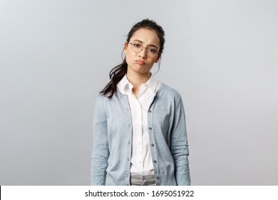 Portrait of sighing displeased and gloomy young asian girl in glasses, pouting and looking disappointed camera, express regret or feel uneasy over failure at work, grey background - Shutterstock ID 1695051922