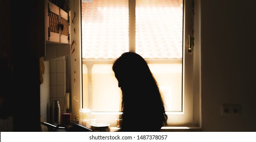 A portrait of a silhouette of an unknown woman with long hair standing in front of a window with rim light from behind the profile - Powered by Shutterstock