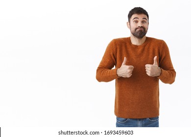 Portrait Of Silly And Handsome Smiling Ordinary Guy, Bearded Man Show Thumb-up And Shrugging, Smirk Say Not Bad, Encourage Friend With Average Normal Result, White Background