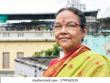 Portrait of a simple looking aged Indian woman in rooftop, holding pair of paper made National Flag of India