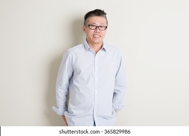 Portrait Of Single Mature 50s Asian Man In Casual Business Arms Crossed And Smiling, Standing Over Plain Background With Shadow.