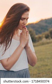 Portrait of a single woman praying and looking down at sunset. Hands folded in prayer concept for faith, spirituality and religion. Peace, hope, dreams concept