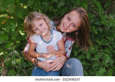 Portrait Of Sisters. Two Beautiful Blond Girls Hugging And Smiling. Children With A Large Age Gap.