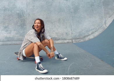 Portrait Of Skater Girl In Skatepark. Female Teenager In Casual Outfit Sitting On Skateboard Against Concrete Wall. Summer Skateboarding With Modern Sport Equipment As Part Of Active Lifestyle. - Powered by Shutterstock