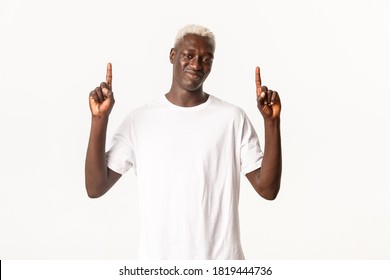 Portrait Of Skeptical Blond African-american Guy Smirk And Pointing Fingers Up, Showing Logo, Standing White Background