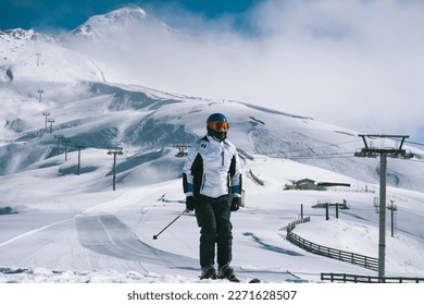 Portrait skier at ski resort standing on sunny day against backdrop of beautiful mountain peaks in the clouds and ski lift