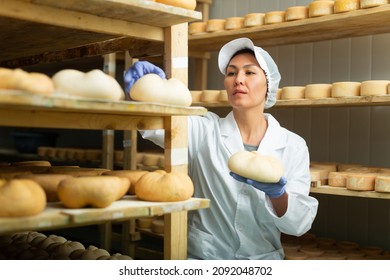 Portrait of skilled Asian woman working in storehouse at cheese factory, controlling maturing process of goat cheese wheels placed on shelves - Powered by Shutterstock