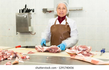 Portrait of skilled female worker cutting raw meat in meat packing factory