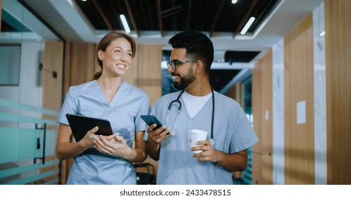 Portrait of skilled happy doctors walking in modern hospital hallways smiling and talking about their jobs. Caucasian doctor and young cheerful male Indian nurse having coffee. - Powered by Shutterstock