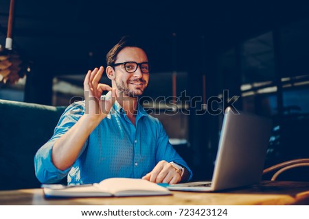 Portrait of skilled male freelancer showing ok sign completing working on project satisfied with salary.successful male IT developer earning money online doing distance job with free schedule