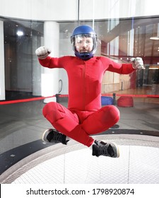 Portrait Of A Skydiver In A Red Uniform And A Helmet In A Wind Tunnel, Sitting In The Air With His Legs Crossed, Flying Without A Parachute Indoors