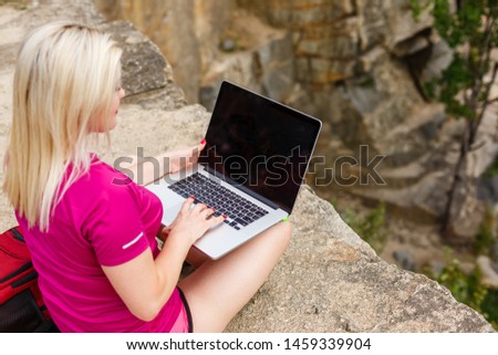 Portrait of a slender young woman on stones near sea. beautiful girl is resting on coast, enjoying outdoor recreation, holding a laptop in her hands, using Internet for business.