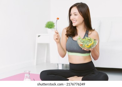 Portrait of slim beautiful Asian woman enjoying heathy salad while sitting on yoga mat at home. Healthy food concept Beautiful Korean or Japanese fit woman eating healthy salad after fitness workout. - Powered by Shutterstock