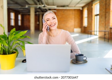 Portrait Of A Slim Beautiful Blonde Woman, 45 Years Old, Smiling. Architect Talking On Cell Phone In Empty Office Over Red Brick Wall Background.