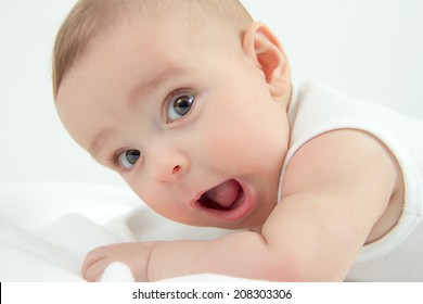 Portrait of a small baby boy in white undershirt lying on his belly with open eyes joyfully yelling and smiling