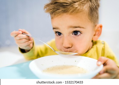 Portrait Of Small Boy Child Eating Soup Meal Or Breakfast Having Lunch By The Table At Home With Spoon White