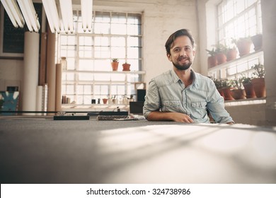 Portrait of a small business owner sitting casually in his worskhop studio looking confident and positive - Shutterstock ID 324738986