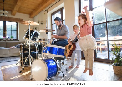 Portrait of small children with father indoors at home, playing drums.