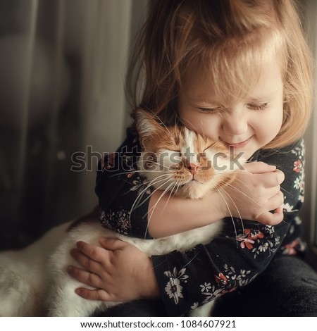 Portrait of a small cute child with a bald head that embraces with tenderness and love a red cat and smiles with happiness