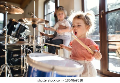 Portrait of small girl indoors at home, playing drums.