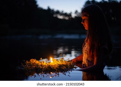 Portrait of a small girl in river late at night, set the wreath to float with a candle. Ivan Kupala tradition in Ukraine