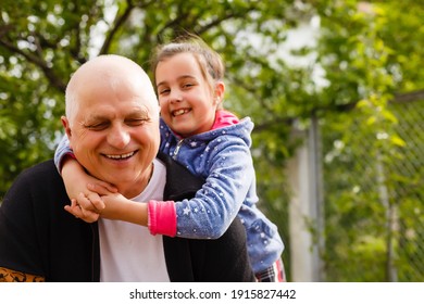Portrait of small girl with senior grandfather in the backyard garden, standing.