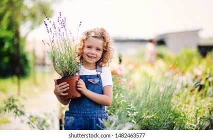 Portrait of small girl standing in the backyard garden, holding a plant in a pot. - Powered by Shutterstock