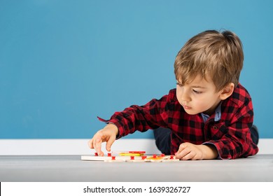 Portrait of small little caucasian boy young child kid laying in front of the blue wall background wearing red and black shirt in studio playing with puzzle toy at home