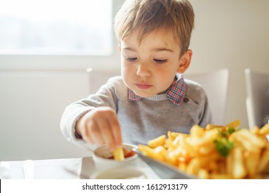 Portrait Of Small Little Cute Caucasian Boy Kid Eating French Fries Potato Chips At The Table In The Restaurant Or At Home Three Or Four Years Old