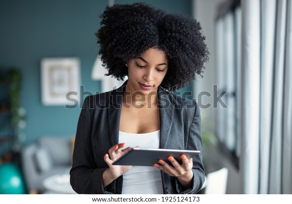 Portrait of smart\
afro young entrepreneur woman using her digital tablet while\
standing in the office at\
home.