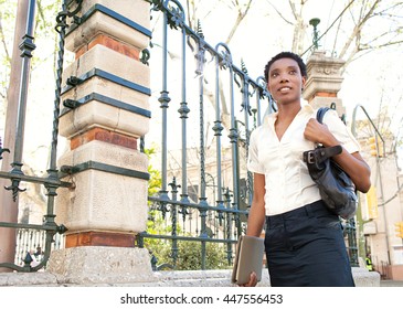 Portrait of a smart black business woman walking in a classic city street with decorative iron work fence, smiling confidently outdoors. Elegant professional woman, lifestyle financial exterior. - Shutterstock ID 447556453