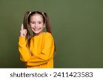 Portrait of smart clever small kid with tails dressed yellow sweatshirt raising finer up has idea isolated on khaki color background