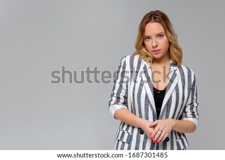 Portrait of smart cunning young woman with fair hair in casual beige blouse standing with sly expression, scheming planning devious tricks, cheating. indoor studio shot